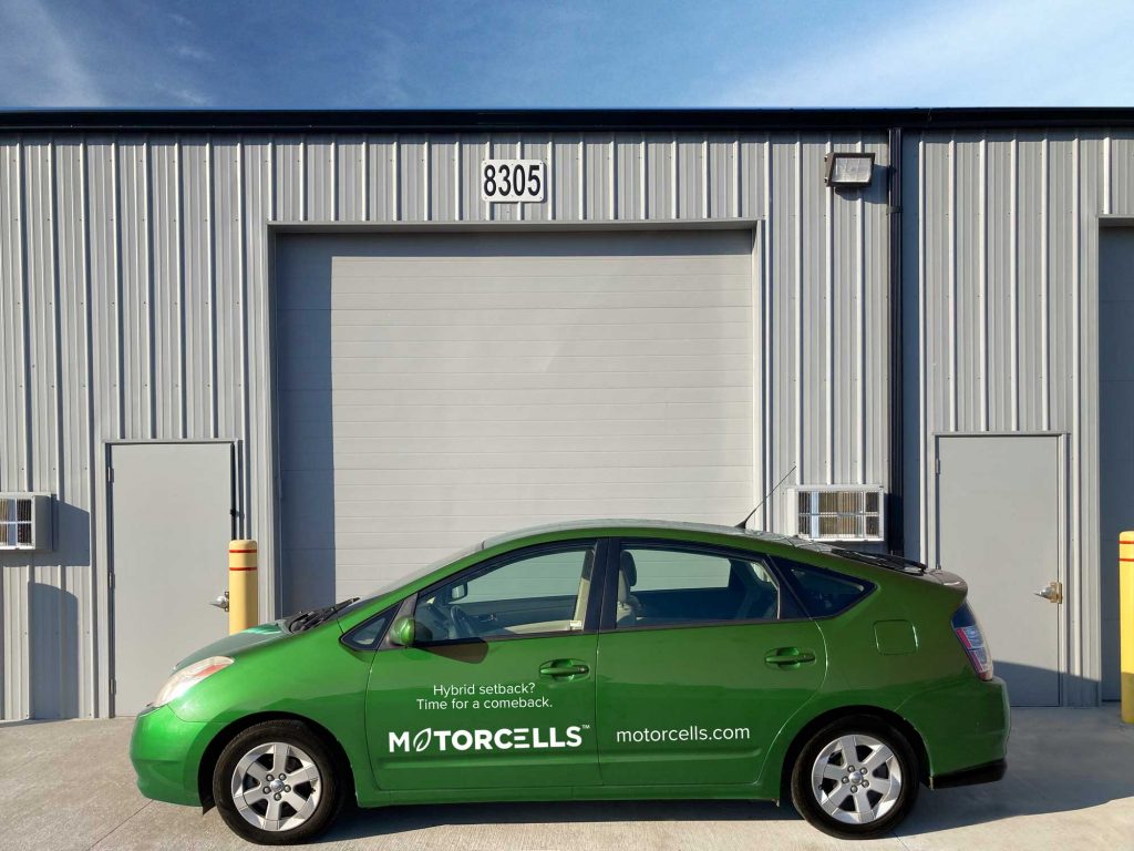 A Motorcells wrapped prius next to the Motorcells garage.